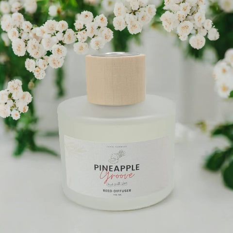 Reed diffuser labeled 'Pineapple Groove' with white flowers in the background