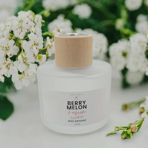 Reed diffuser with a wooden cap surrounded by white flowers on a light surface