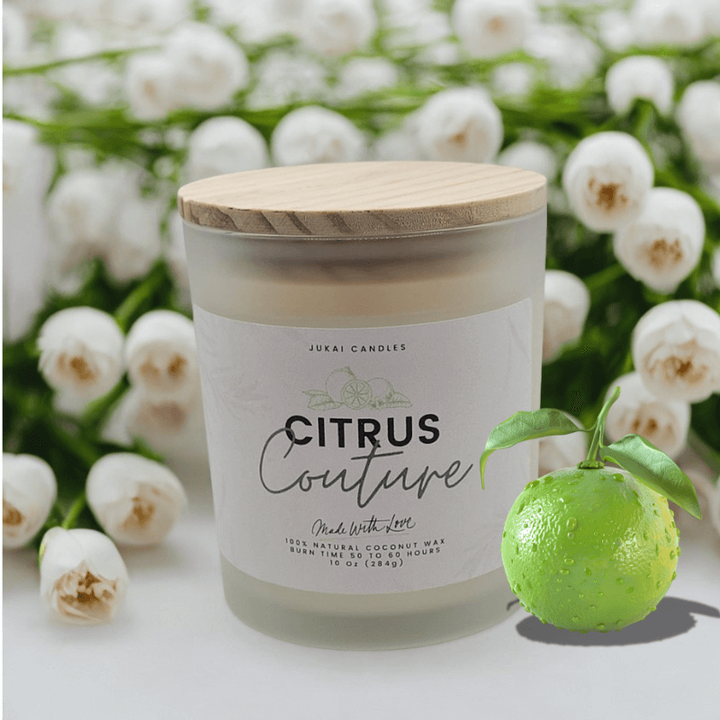 Candle labeled 'Citrus Couture' with a wooden lid, surrounded by white flowers and a lime.