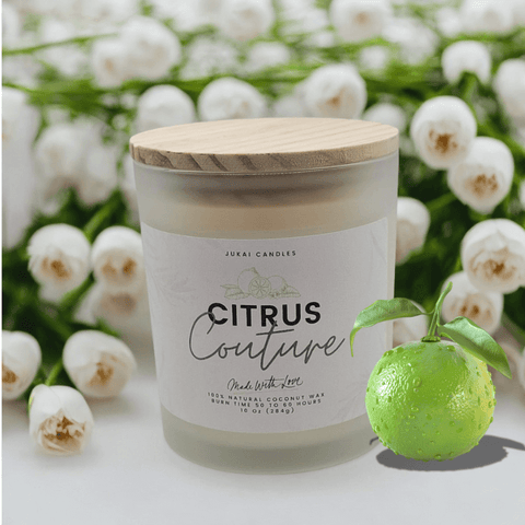 Candle labeled 'Citrus Couture' with a wooden lid, surrounded by white flowers and a lime.