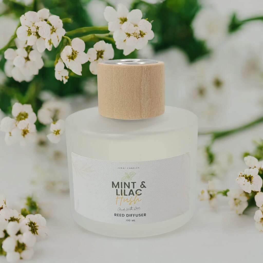 Reed diffuser with a wooden cap surrounded by white flowers on a light background
