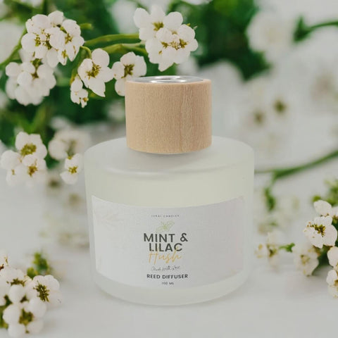 Reed diffuser with a wooden cap surrounded by white flowers on a light background
