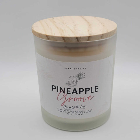 Candle with a wooden lid labeled 'Pineapple Groove' by Jukai Candles on a light gray background